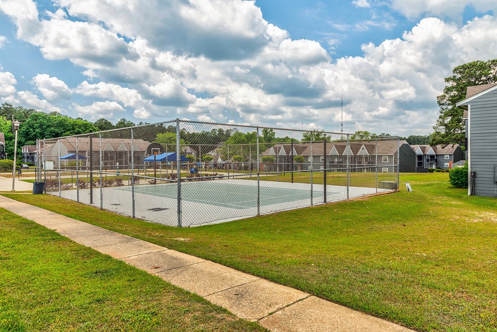 a fenced in tennis court with a volleyball court in front of houses