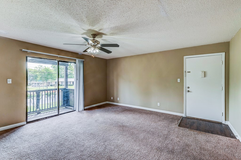 an empty living room with a ceiling fan and a door to a balcony
