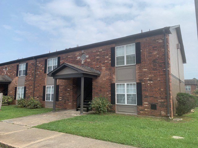 a brick apartment building with a green lawn and blue sky in the background