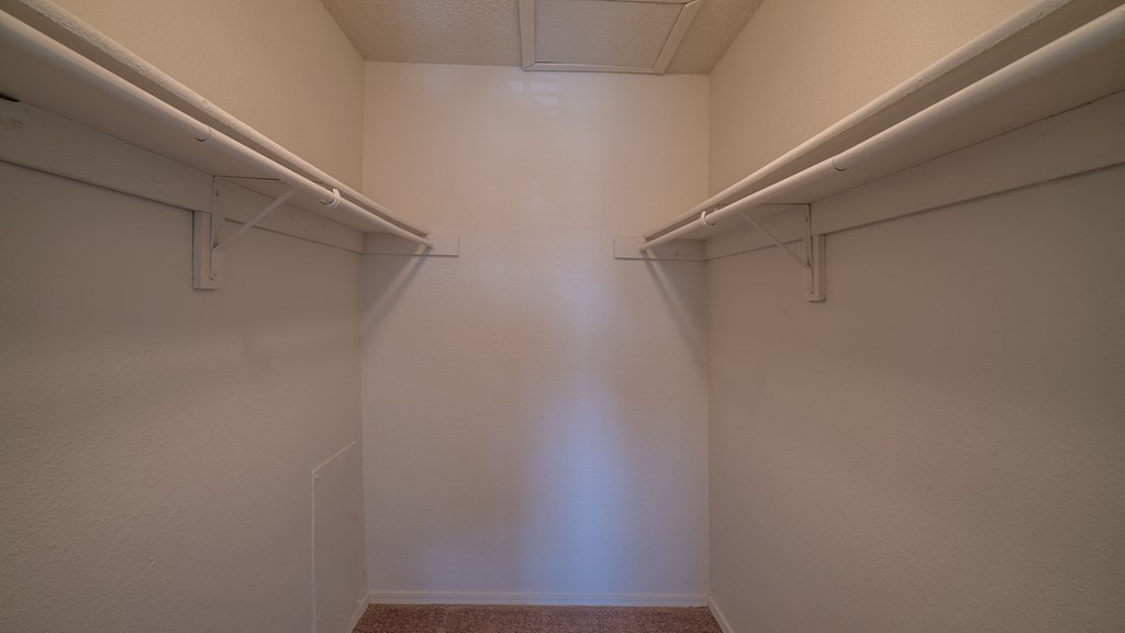 a walk in closet with two white walls and two hanging rails