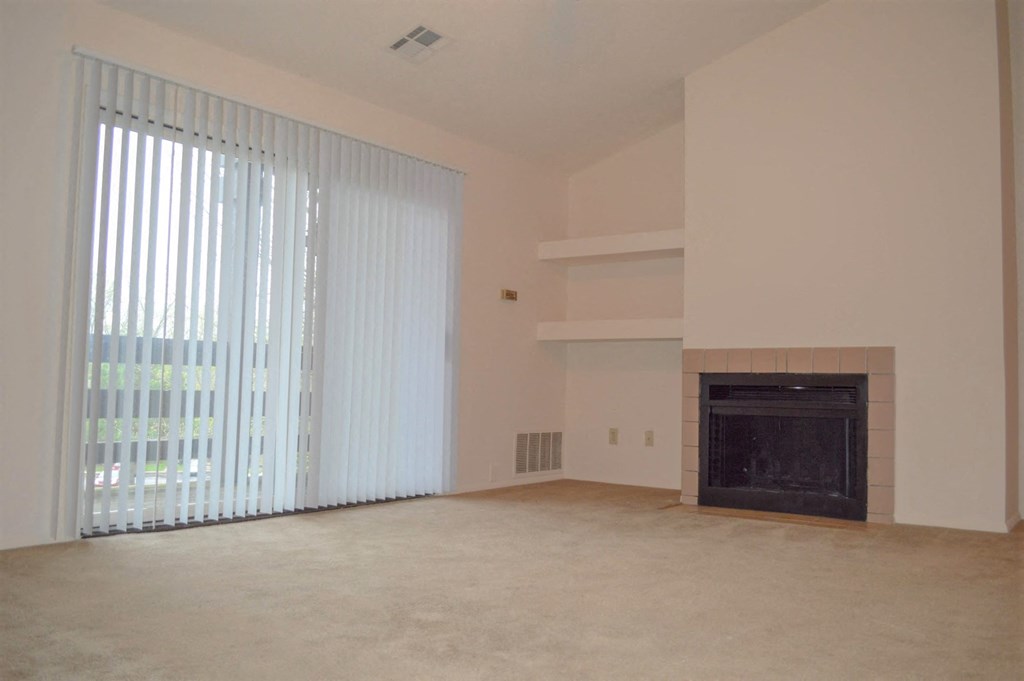 an empty living room with a fireplace and blinds on the window