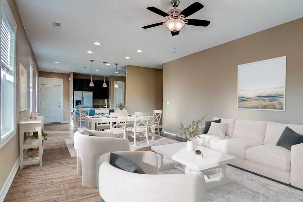 A spacious living room with a white sofa set and a ceiling fan.