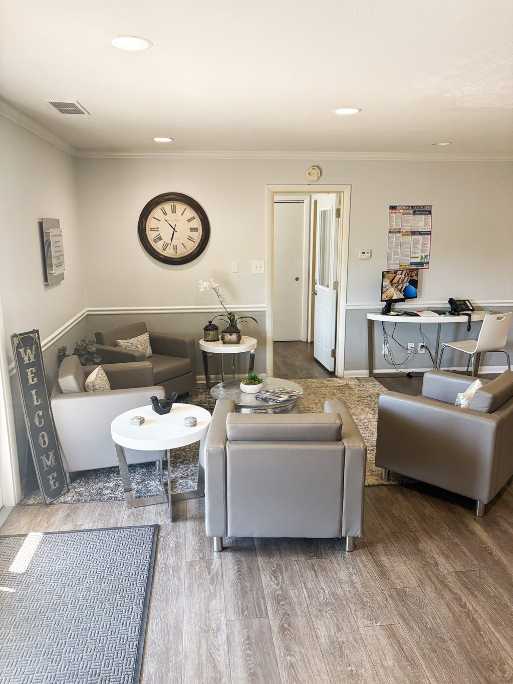 A living room with a grey sofa, a white coffee table, and a large clock on the wall.