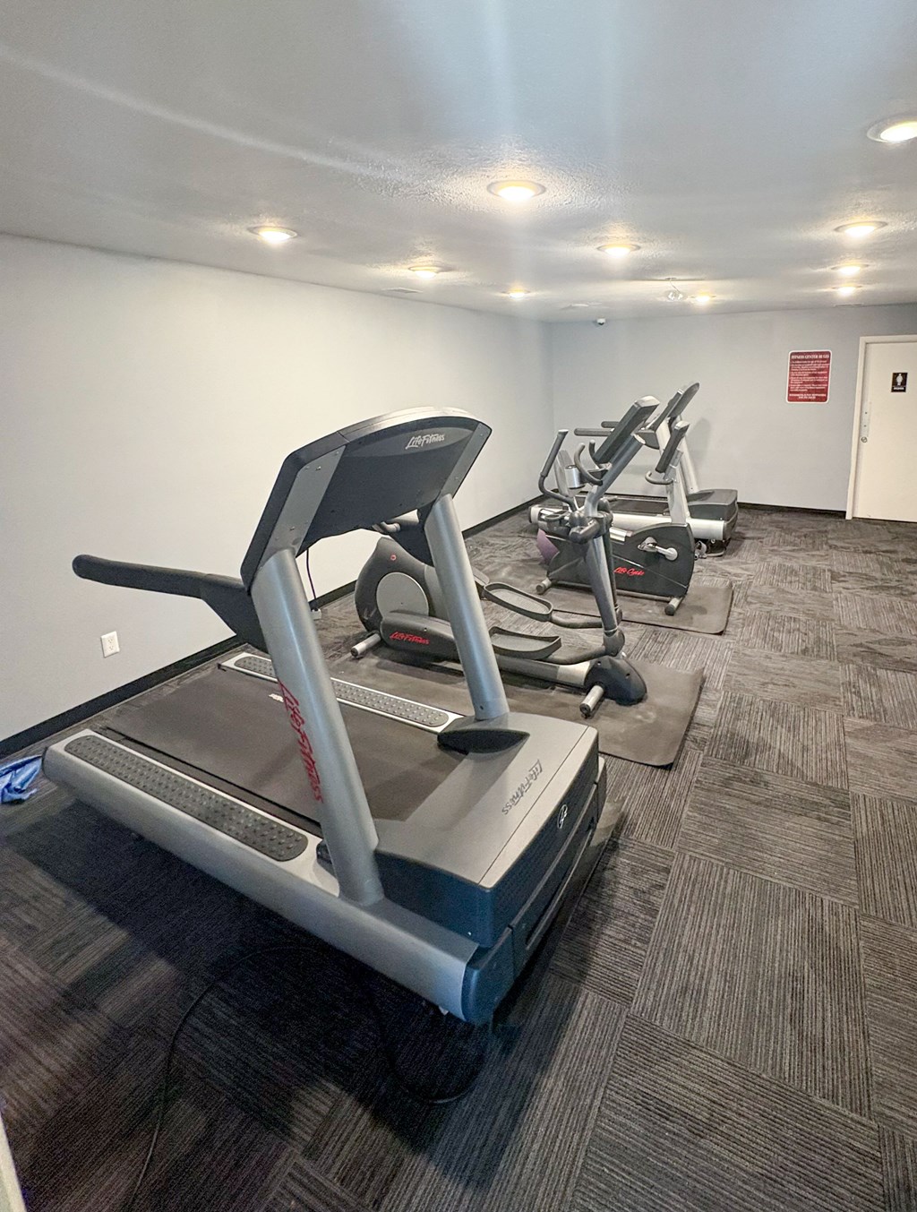 A treadmill in a gym with a grey carpet.
