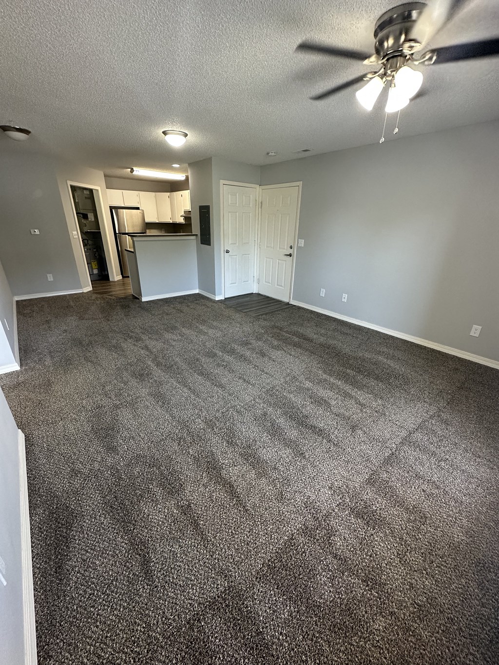 an empty living room with a ceiling fan and a kitchen in the background