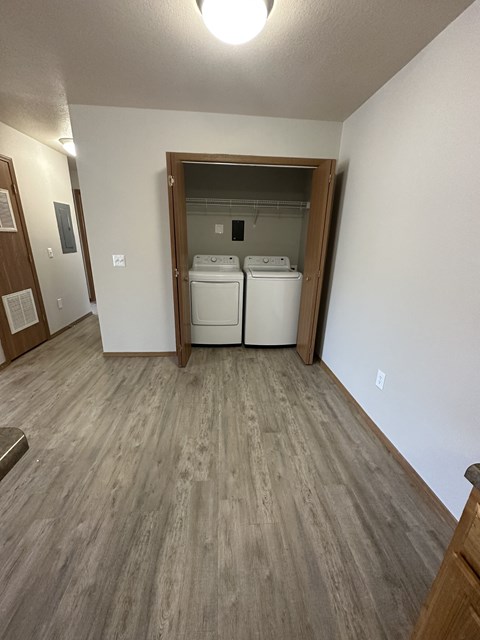 the living room and laundry room of an apartment with wood flooring