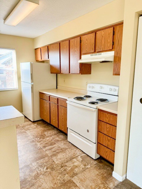 A kitchen with a white stove top oven and wooden cabinets.