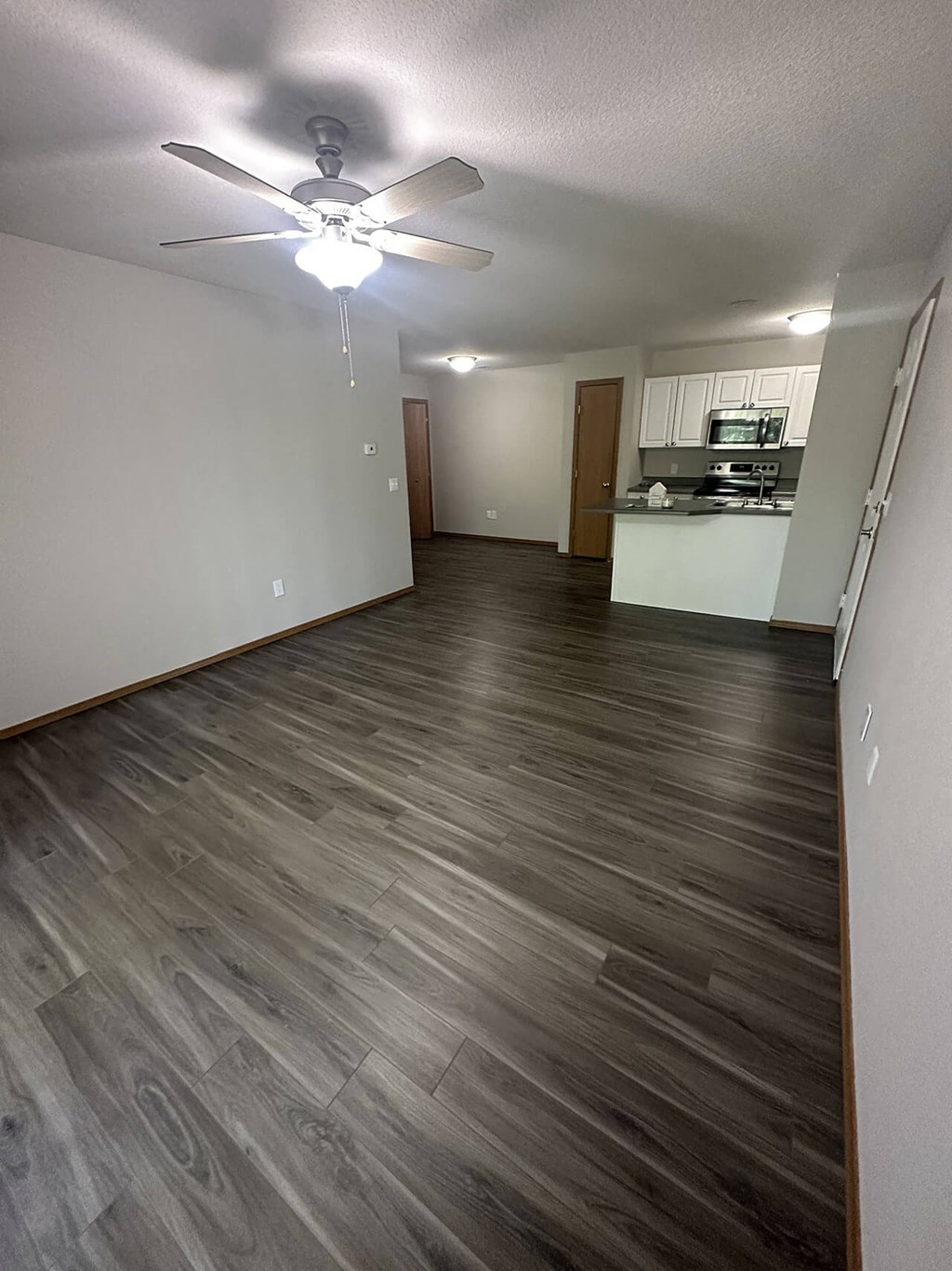 a living room and kitchen with wood flooring and a ceiling fan