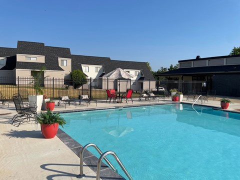 A swimming pool surrounded by chairs and potted plants.