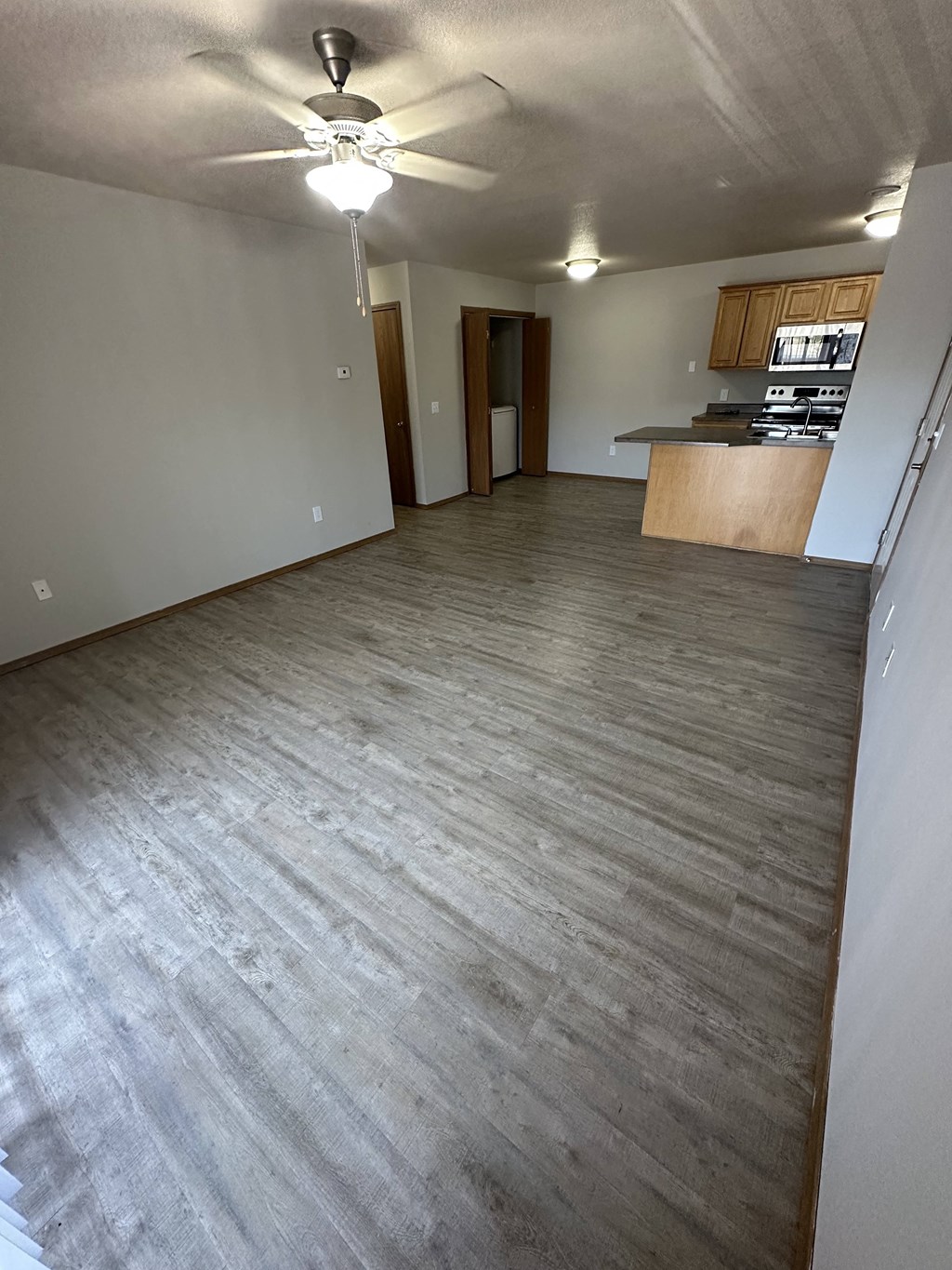 an empty living room with a kitchen in the background