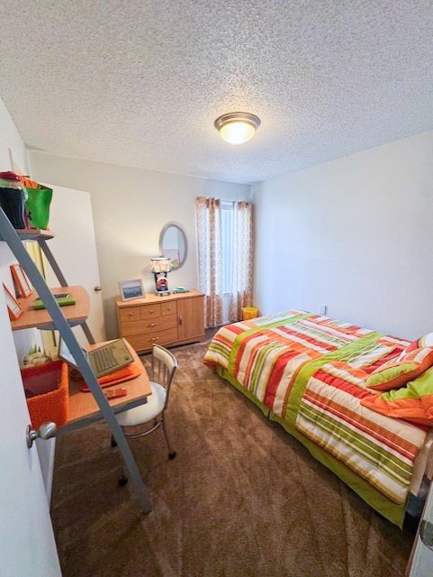 A bedroom with a bed, desk, chair, and a window with curtains.
