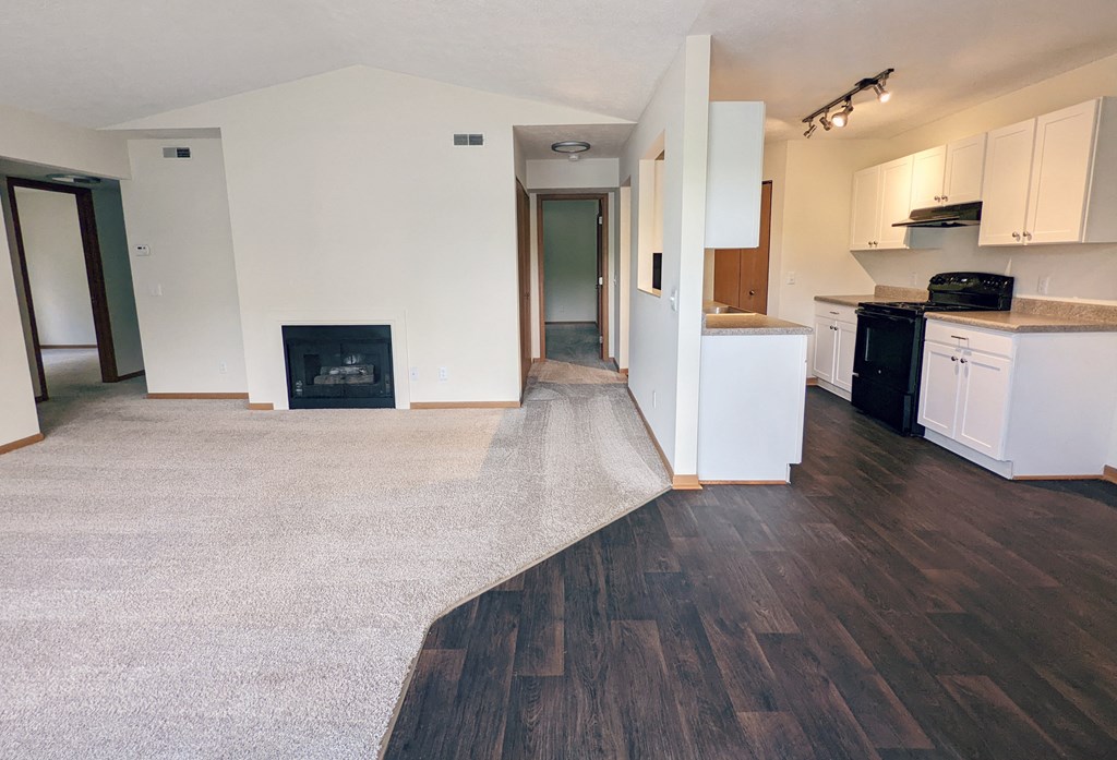 an empty kitchen with white cabinets and wood flooring and a fireplace