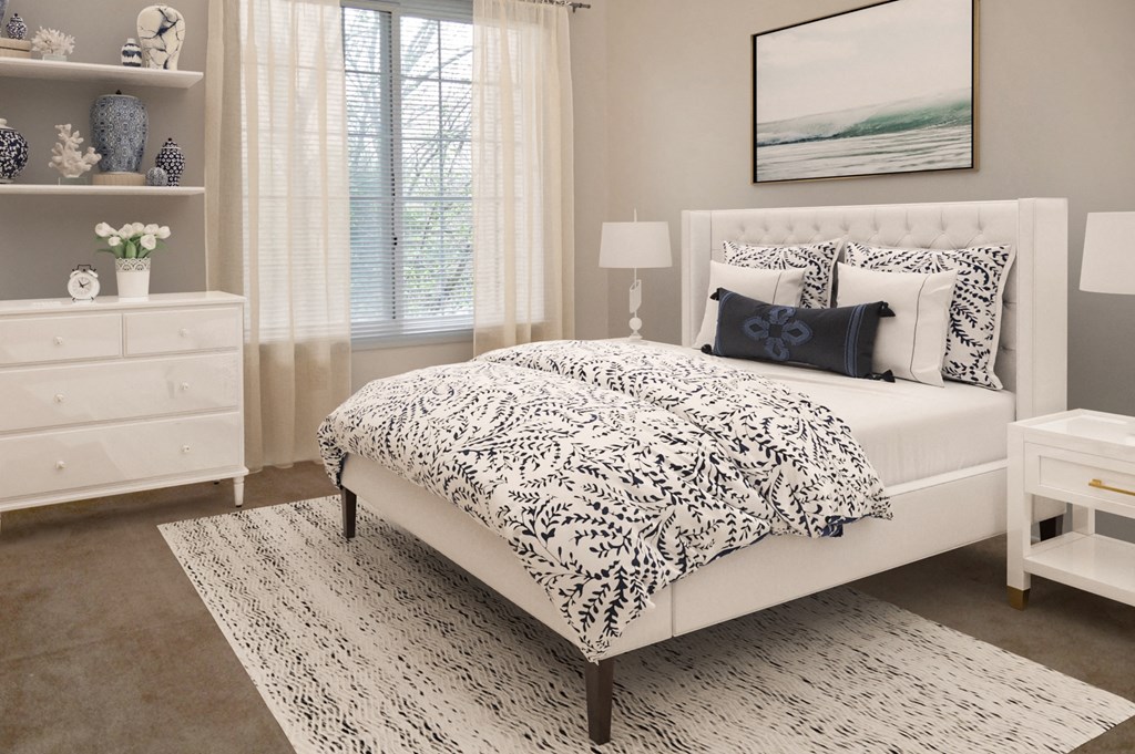A bed with a white and black patterned comforter sits in a room with a white dresser and a small table with a lamp.