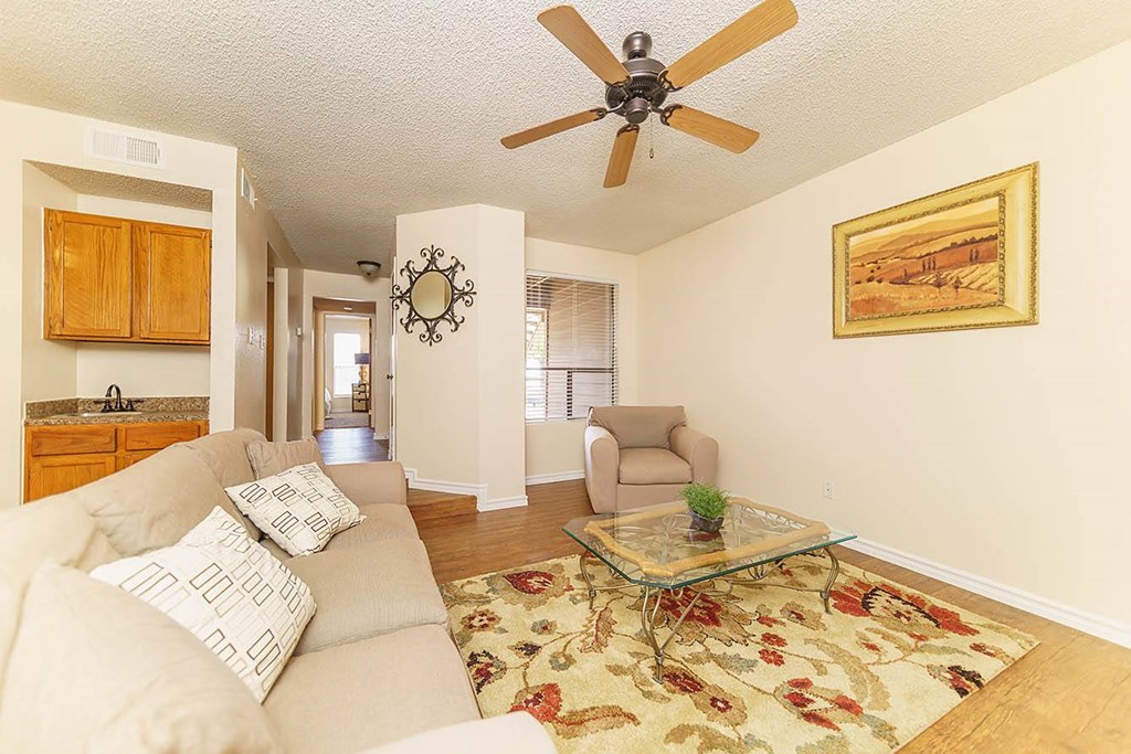 A living room with a beige couch, a glass coffee table, and a ceiling fan.