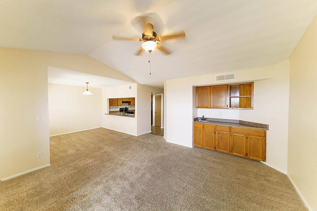 A room with a ceiling fan and a kitchenette in the background.