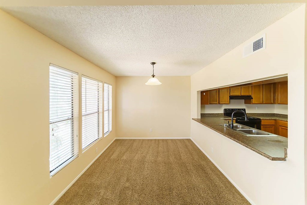 A room with a carpeted floor and a kitchen area in the background.