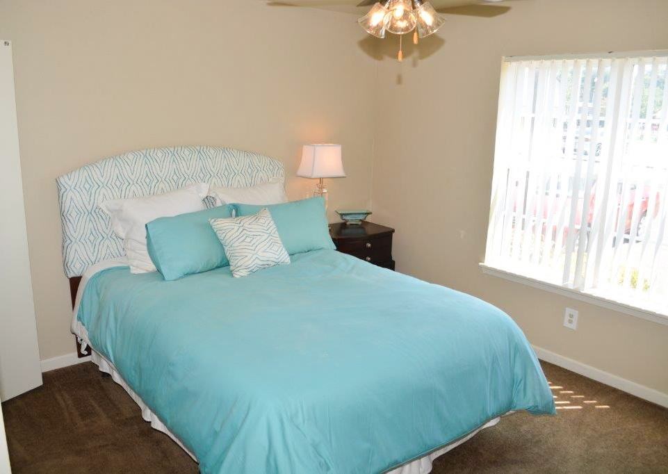 A bed with a blue comforter and pillows is in a room with a ceiling fan and a window.