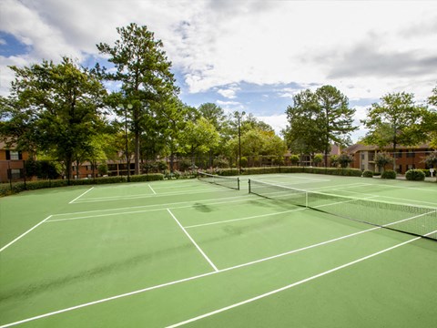 A tennis court surrounded by trees and buildings.