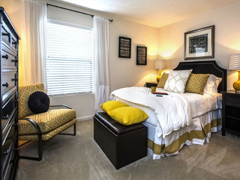 A bedroom with a bed, chair, and nightstand.