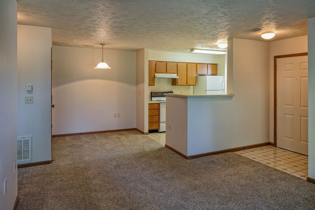 an empty living room with a kitchen in the background