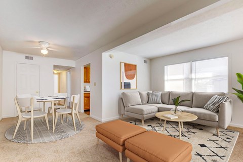 A living room with a white table and chairs, a grey couch, and a brown ottoman.