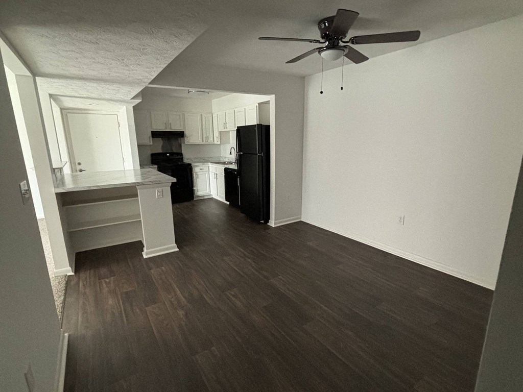 an empty living room and kitchen with wood floors and a ceiling fan