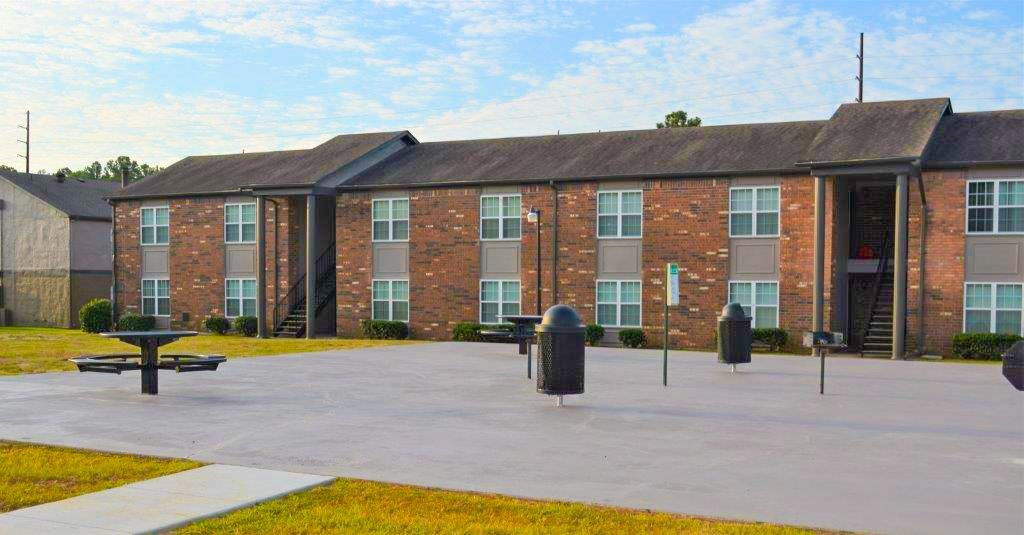 A brick building with a black roof and a parking lot in front.