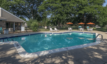 a pool with chairs and umbrellas in front of a house