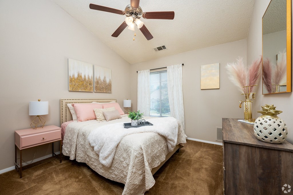 A bedroom with a bed, a pink table, and a ceiling fan.