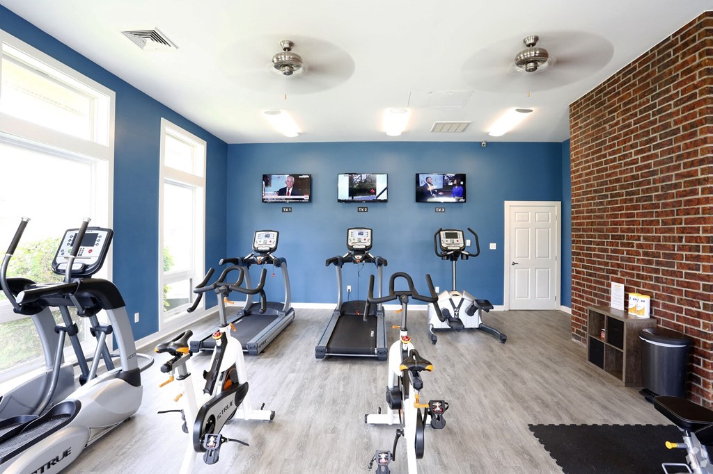 A gym with a variety of cardio equipment and a brick wall.