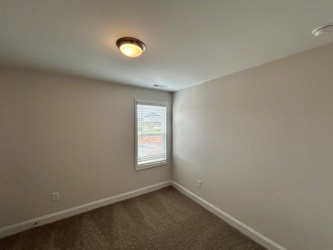A room with a carpeted floor and a window with blinds.