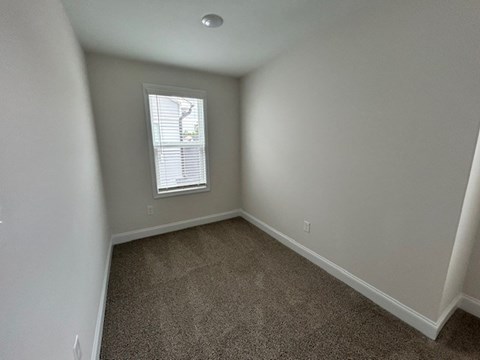A room with a carpeted floor and a window with blinds.