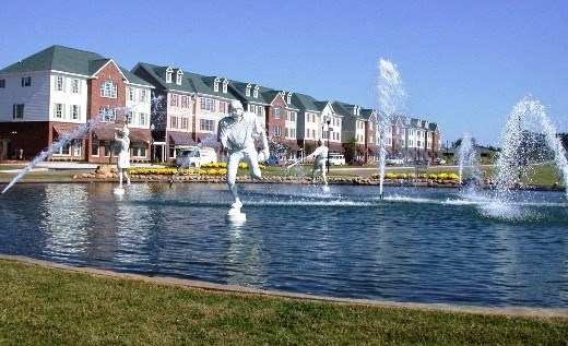 a fountain in the middle of a lake with houses in the background