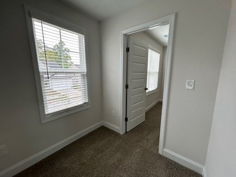 A room with a carpeted floor, a window with blinds, and a door.