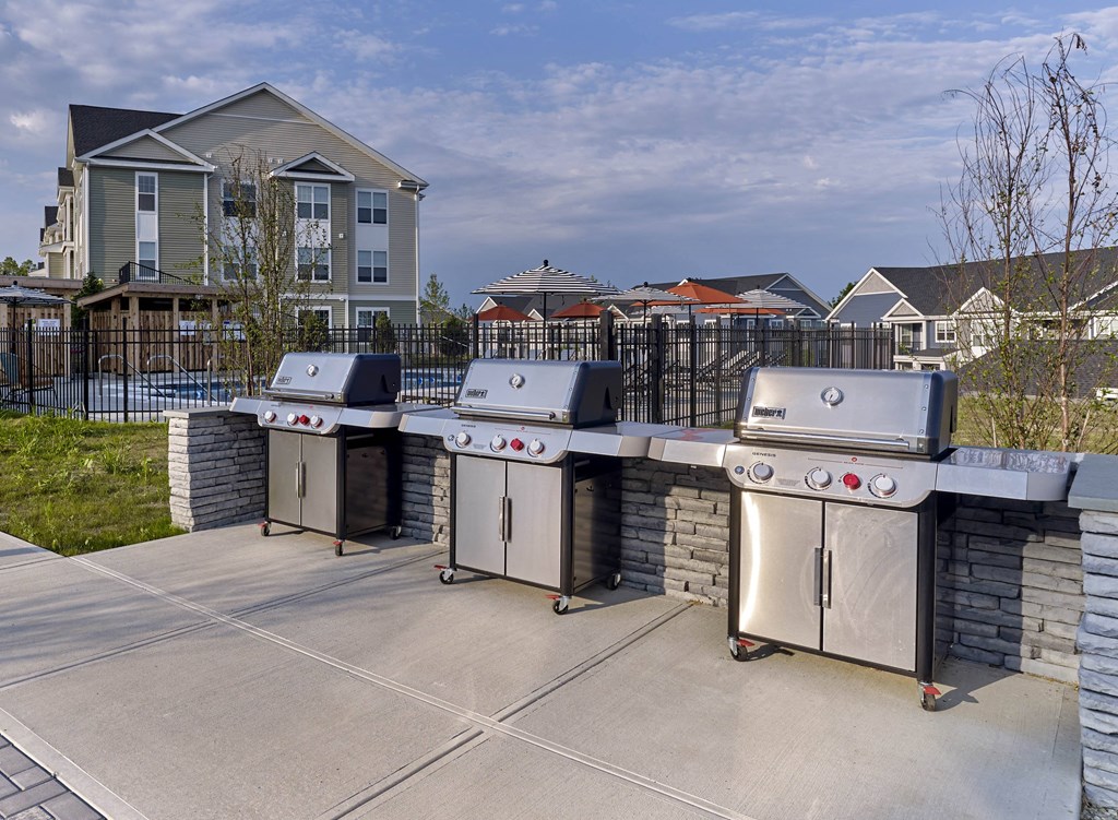three stainless steel barbecue grills on a patio with houses in the background