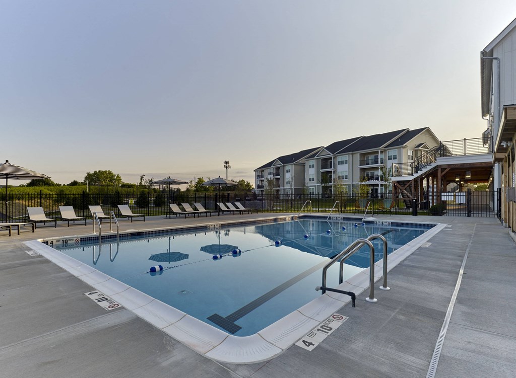 a swimming pool with chairs around it in front of an apartment building