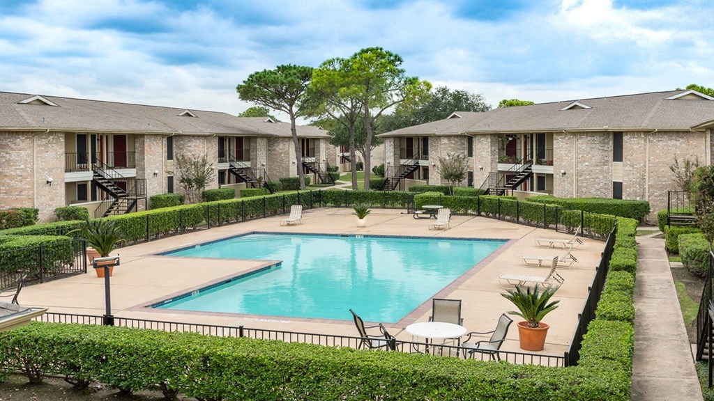 a swimming pool with chairs around it in front of apartments