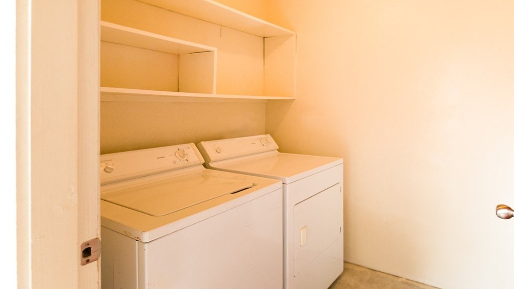 a washer and dryer in an empty laundry room with shelves