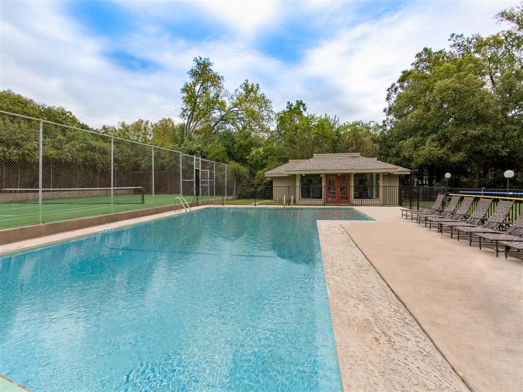 a swimming pool with a tennis court and a house in the background