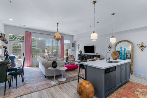 A modern kitchen with a grey island and a living room with a sofa and a TV.