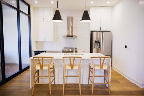 A kitchen with a white counter top and wooden bar stools.