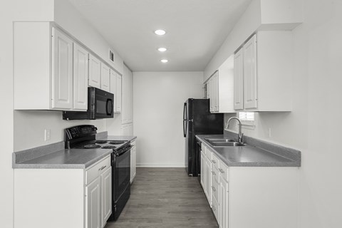 A black refrigerator sits in a kitchen with white cabinets.