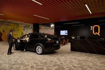 A black car is parked in a showroom with a man standing beside it.