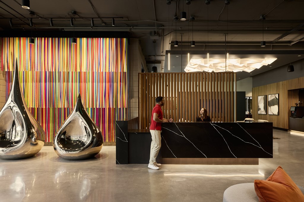 A man in a red shirt and white pants stands in front of a reception desk.