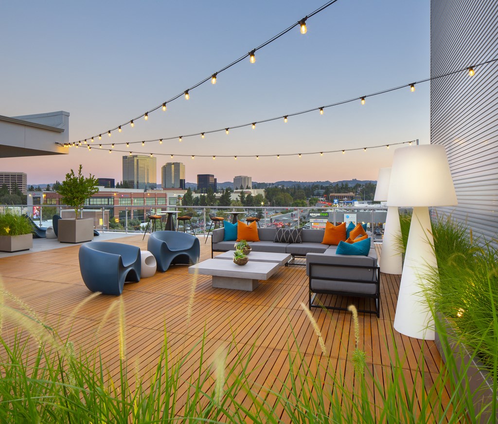 a roof deck with couches and chairs and a city in the background
