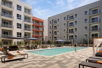 A woman is standing in the pool area of a hotel with a pool, sun loungers and umbrellas.