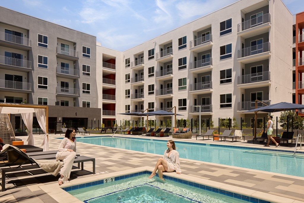 Two women are sitting by a pool in front of apartment buildings.