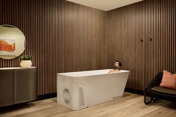 A man is sitting in a white bathtub in a room with wooden walls.