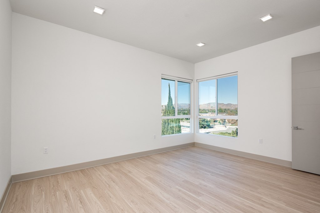 a living room with white walls and wooden floors and large windows