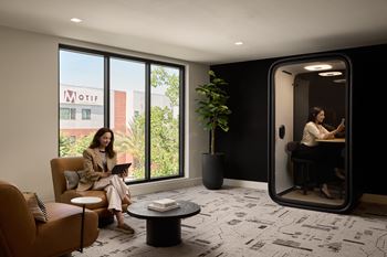 A woman is sitting on a couch in a room with a large window and a plant.